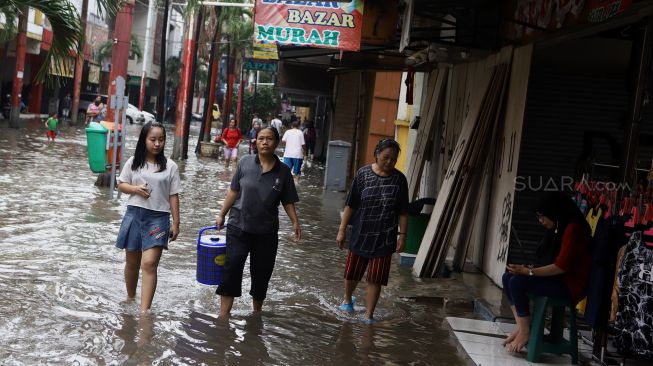 Sejumlah warga melintasi banjir yang merendam kawasan Pasar Baru, Jakarta Pusat, Selasa (25/2).  [Suara.com/Angga Budhiyanto]