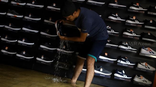 Seorang pekerja memeras salah satu sepatu di dalam toko sepatu saat banjir merendam kawasan Pasar Baru, Jakarta Pusat, Selasa (25/2). [Suara.com/Angga Budhiyanto]
