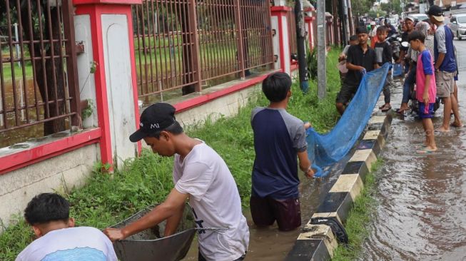 Warga mencari ikan di pinggir Jalan Jati Makmur yang tergenang banjir di Bekasi, Jawa Barat, Selasa (25/02). [Suara.com/Alfian Winanto]