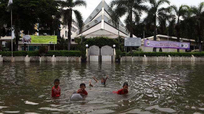 Sejumlah anak bermain di depan Gereja Santo Kristoforus yang terendam banjir di kawasan Jalan Satria IV, Kelurahan Jelambar, Jakarta Barat, Selasa (25/2). [Suara.com/Angga Budhiyanto]  