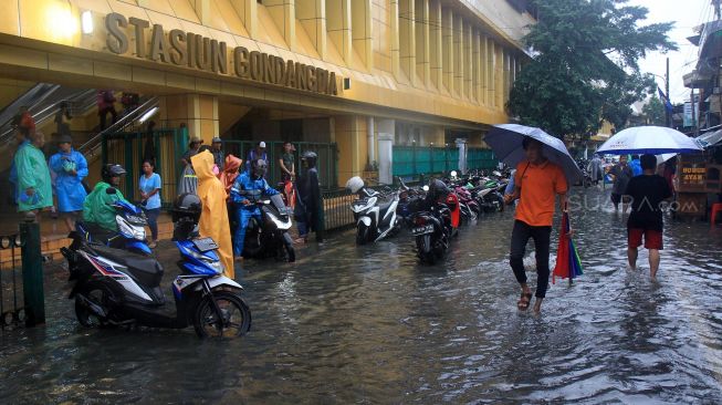 Warga melintasi genangan air di Stasiun Gondangdia, Jakarta, Selasa (25/2). [Suara.com/Oke Atmaja]
