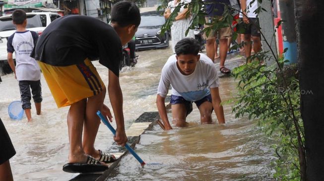 Warga mencari ikan di pinggir Jalan Jati Makmur yang tergenang banjir di Bekasi, Jawa Barat, Selasa (25/02). [Suara.com/Alfian Winanto]