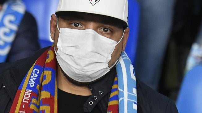 Seorang suporter Napoli mengenakan masker menunggu dimulainya pertandingan Napoli vs Barcelona di Stadion San Paolo, Naples, Italia, Rabu (26/2) dini hari WIB.  [Filippo MONTEFORTE / AFP]