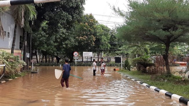 Sejumlah anak-anak tampak asik bermain di lokasi banjir, sekitar Perumahan Bumi Nasio Indah, Jalan Raya Jatimekar, Jatiasih, Bekasi, Jawa Barat, Rabu (26/2/2020). (Suara.com/Ummi Saleh)