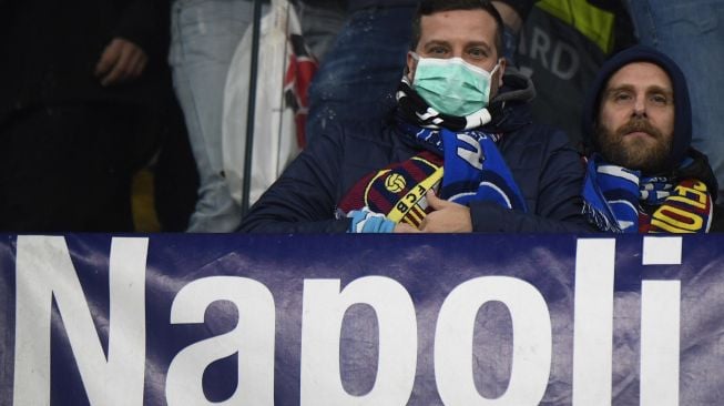 Suporter Napoli mengenakan masker menunggu dimulainya pertandingan Napoli vs Barcelona di Stadion San Paolo, Naples, Italia, Rabu (26/2) dini hari WIB.  [Filippo MONTEFORTE / AFP]