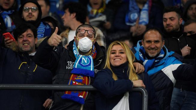 Seorang suporter Napoli mengenakan masker sambil menunggu dimulainya pertandingan Napoli vs Barcelona di Stadion San Paolo, Naples, Italia, Rabu (26/2) dini hari WIB.  [Filippo MONTEFORTE / AFP]