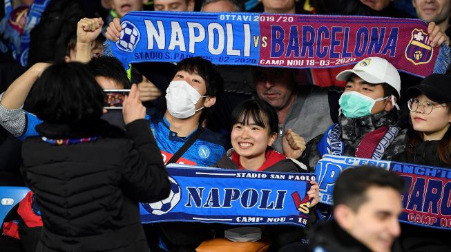 Seorang suporter Napoli mengenakan masker menunggu dimulainya pertandingan Napoli vs Barcelona di Stadion San Paolo, Naples, Italia, Rabu (26/2) dini hari WIB.  [Filippo MONTEFORTE / AFP]
