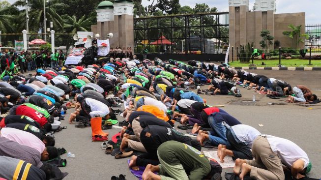 Para pengemudi Ojol (Ojek Online) bersujud saat Salat Jumat bareng Polisi di depan Gedung  DPR dan MPR RI, Jakarta, Jumat (28/02). [Suara.com/Alfian Winanto]
