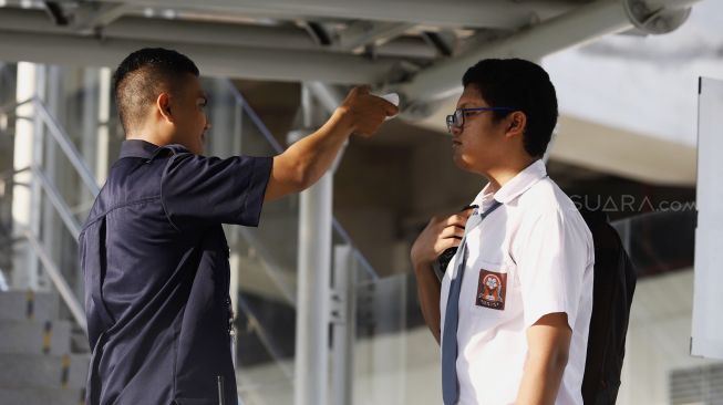 Petugas meriksa suhu tubuh seorang pelajar calon penumpang sebelum memasuki Stasiun LRT Velodrome, Rawamangun, Jakarta Timur, Selasa (3/3). [Suara.com/Angga Budhiyanto]