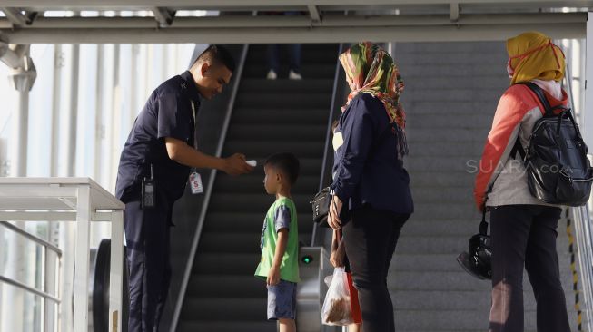 Petugas meriksa suhu tubuh seorang anak kecil calon penumpang sebelum memasuki Stasiun LRT Velodrome, Rawamangun, Jakarta Timur, Selasa (3/3). [Suara.com/Angga Budhiyanto]