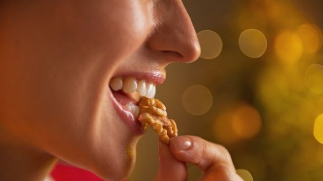Seorang perempuan sedang menikmati kacang kenari. [Shutterstock]