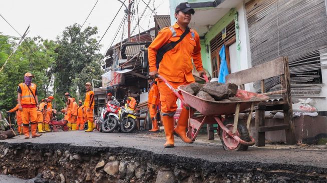 Petugas memindahkan batu dengan alat di Jalan Kesatrian X RT.12/3, Matraman, Jakarta Timur, Kamis (5/3). [Suara.com/Alfian Winanto]