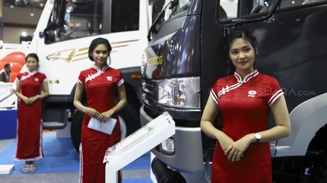 Tiga model berpose di depan truk yang dipamerkan di pameran otomotif GAIKINDO Indonesia International Commercial Vehicle Expo (GIICOMVEC) di Jakarta Convention Center (JCC), Jakarta, Kamis (5/3). [Suara.com/Angga Budhiyanto]