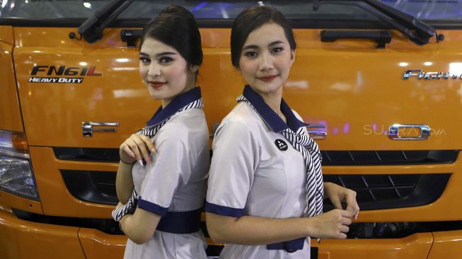 Dua model berpose di depan truk yang dipamerkan di pameran otomotif GAIKINDO Indonesia International Commercial Vehicle Expo (GIICOMVEC) di Jakarta Convention Center (JCC), Jakarta, Kamis (5/3). [Suara.com/Angga Budhiyanto]
