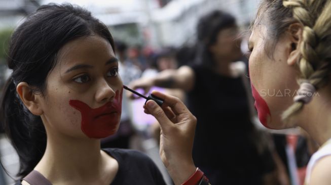 Massa yang tergabung dalam Aliansi Gerakan Perempuan Anti-Kekerasan (GERAK Perempuan) melukis wajahnya saat melakukan aksi unjuk rasa di depan kantor Bawaslu, Jakarta, Minggu (8/3). [Suara.com/Angga Budhiyanto]