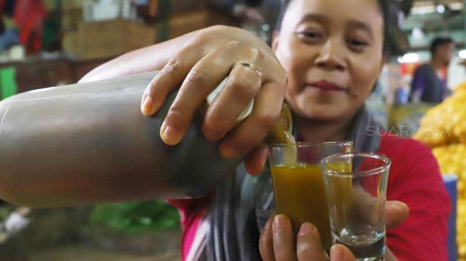 Ibu Endang menuang jamu kedalam gelas di Pasar Induk, Kramat Jati, Jakarta Timur, Senin (9/3). [Suara.com/Alfian Winanto]