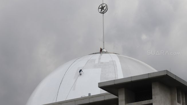 Pekerja dengan pengaman lengkap melakukan pengecatan pada bagian kubah Masjid Istiqlal, Jakarta, Selasa (10/3).  [Suara.com/Angga Budhiyanto]
