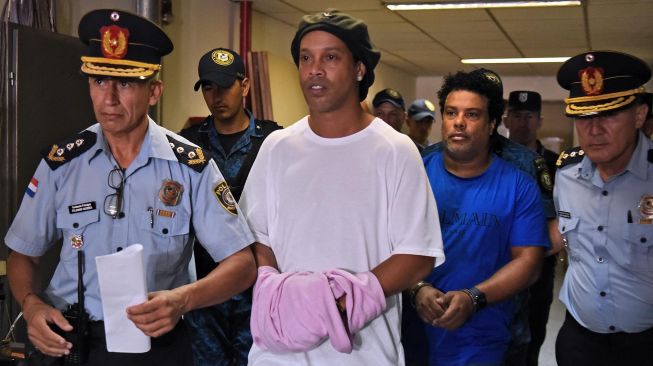 Mantan pemain timnas Brasil, Ronaldinho dikawal oleh polisi meninggalkan kantor pengadilan di Asuncion, ibu kota Paraguay, Sabtu (7/3). [Foto AFP]