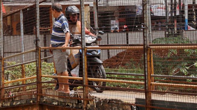 Sejumlah pengguna kendaraan bermotor melintasi jembatan penyeberangan orang di jalan K.H Noer Ali Kalimalang, Bekasi, kamis (12/3).  [Suara.com/Alfian Winanto]