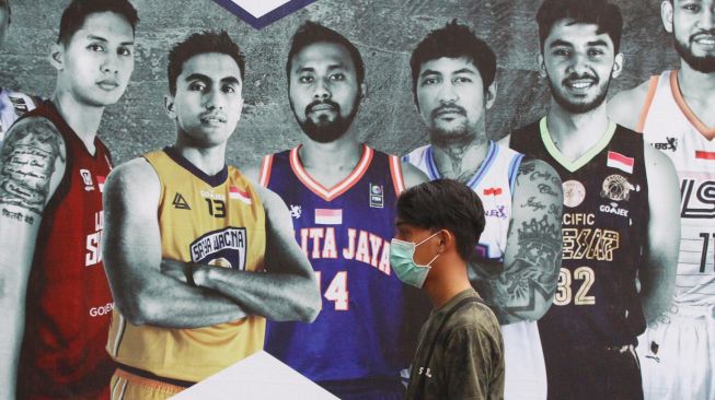 Seorang penonton yang mengenakan masker melintas di depan baliho Indonesia Basketball League (IBL) 2020 Seri VII di GOR Bimasakti, Malang, Jawa Timur, Jumat (13/3). [ANTARA FOTO/Ari Bowo Sucipto]