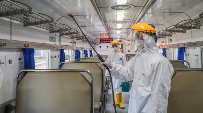 Petugas menyemprotkan cairan disinfektan di langit-langit gerbong kereta di Stasiun Pasar Senen, Jakarta, Minggu (15/3/2020).[Suara.com/Alfian Winanto]