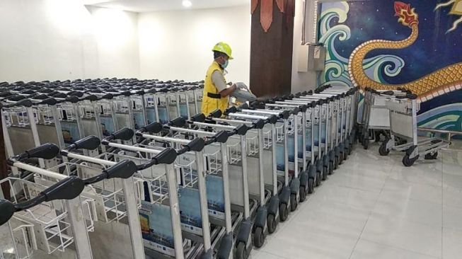 Petugas Health Quarantine dari KKP Kelas IV menyemprot disinfektan di barisan troli yang ada di Bandara Adisutjipto, Yogyakarta, Senin (16/3/2020). - (SuaraJogja.id/Muhammad Ilham Baktora)