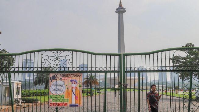 Warga melintas di kawasan Monas di Jakarta, Senin (16/3).  [Suara.com/Alfian Winanto]