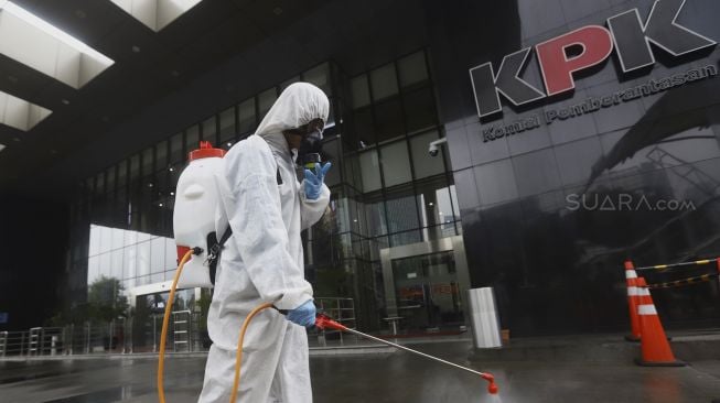 Petugas menyemprotkan cairan disinfektan pada bagian jalan gedung KPK, Jakarta, Rabu (18/3).[Suara.com/Angga Budhiyanto]