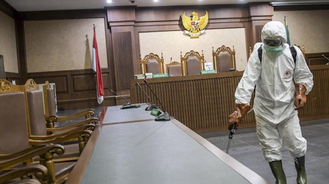 Petugas PMI Kota Jakarta Pusat menyemprotkan cairan disinfektan di kolong meja ruangan sidang Pengadilan Tipikor, Jakarta, Rabu (18/3).   [ANTARA FOTO/Galih Pradipta]