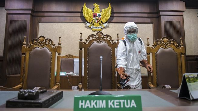 Petugas PMI Kota Jakarta Pusat menyemprotkan cairan disinfektan di ruangan sidang Pengadilan Tipikor, Jakarta, Rabu (18/3).   [ANTARA FOTO/Galih Pradipta]