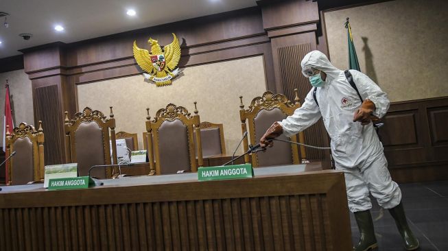 Petugas PMI Kota Jakarta Pusat menyemprotkan cairan disinfektan di meja hakim ruangan sidang Pengadilan Tipikor, Jakarta, Rabu (18/3).   [ANTARA FOTO/Galih Pradipta]