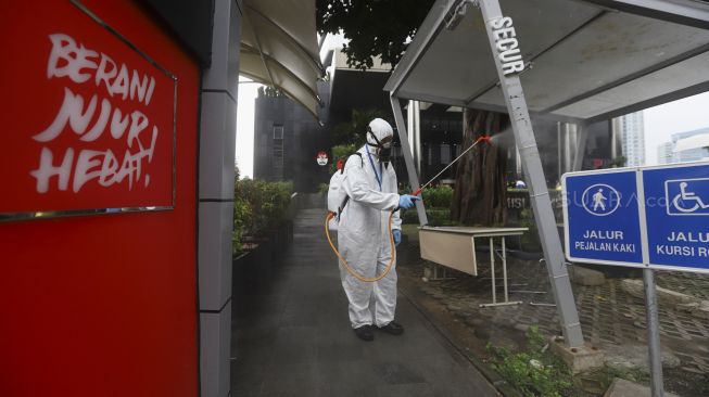 Petugas menyemprotkan cairan disinfektan pada bagian tiang gedung KPK, Jakarta, Rabu (18/3).[Suara.com/Angga Budhiyanto]