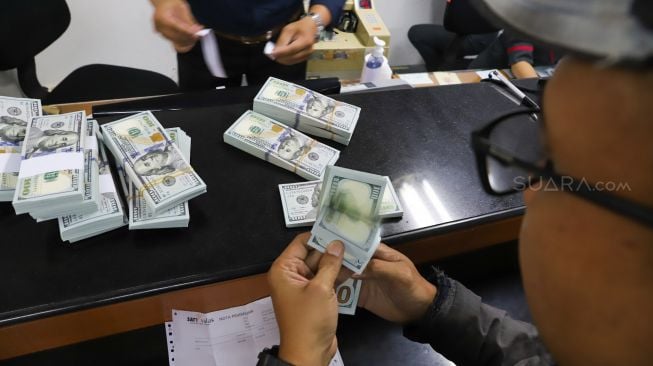 Pembeli menghitung uang dolar di Ayumas Money Changer, Jakarta Pusat, Kamis (19/3). [Suara.com/Alfian Winanto]