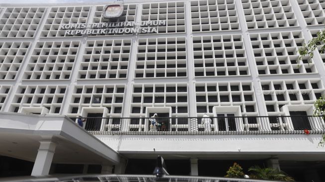 Petugas melakukan penyemprotan cairan disinfektan pada bagian luar gedung Komisi Pemilihan Umum (KPU) Republik Indonesia, Jakarta, Jumat (20/3). [Suara.com/Angga Budhiyanto]