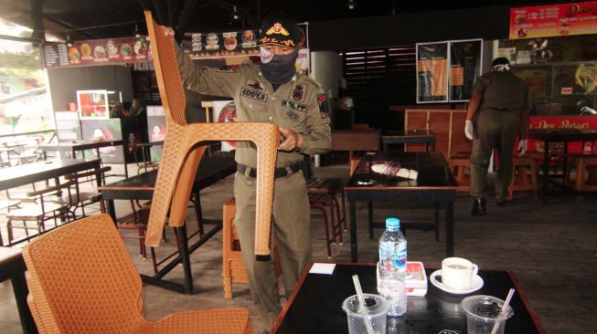 Dua petugas Satpol PP Kota Pontianak mengangkat sejumlah kursi untuk disimpan ke dalam warung kopi saat melakukan penertiban di Pontianak, Kalimantan Barat, Jumat (20/3). [ANTARA FOTO/Jessica Helena Wuysang]