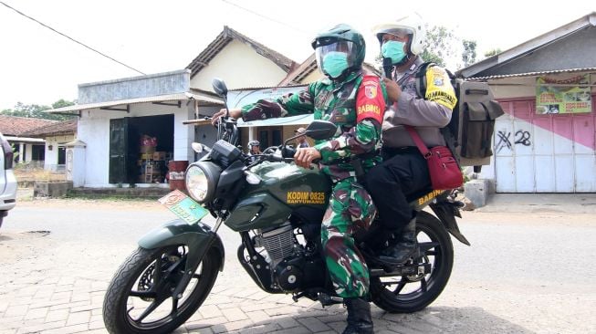 Bripka Indra Bayu (kanan) bersama Sertu Miseli keliling kampung memberikan imbauan pencegahan COVID-19 di Tegal Sari, Banyuwangi, Jawa Timur, Sabtu (21/3).   [ANTARA FOTO/Budi Candra Setya]
