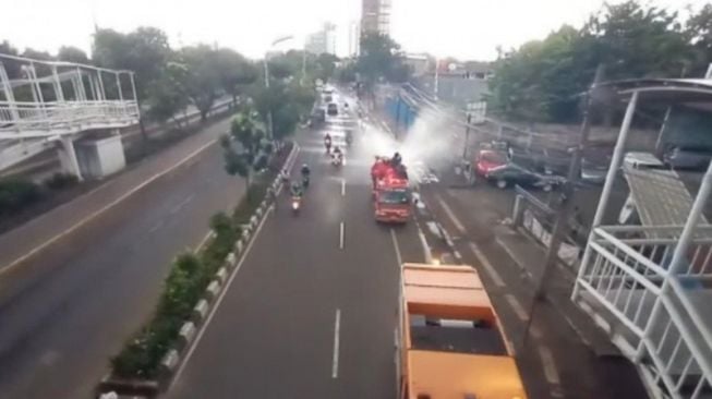 Petugas Pemadam Kebakaran (Damkar) Jakarta Timur menyemprotkan disinfektan di sepanjang jalan protokol di Jakarta, Minggu (22/3/2020). (Antara)