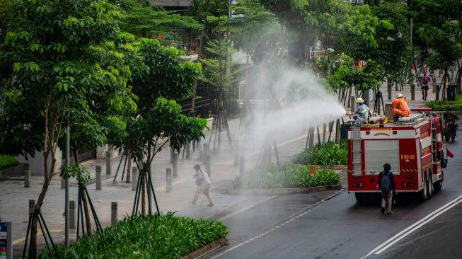 Petugas Damkar menyemprotkan cairan disinfektan di kawasan Jalan Sudirman, Jakarta, Minggu (22/3). [ANTARA FOTO/Aprillio Akbar]