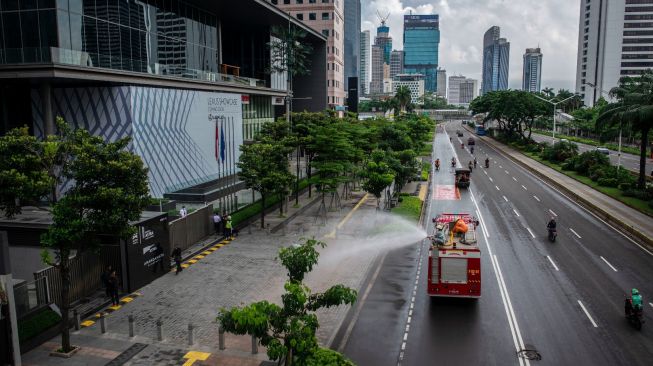 Petugas Damkar menyemprotkan cairan disinfektan di kawasan Jalan Sudirman, Jakarta, Minggu (22/3). [ANTARA FOTO/Aprillio Akbar]