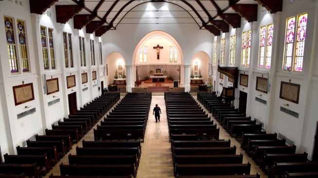 Petugas keamanan gereja melintas diantara kursi kosong di Gereja Katedral Surabaya, Jawa Timur, Minggu (22/3). [ANTARA FOTO/Zabur Karuru]