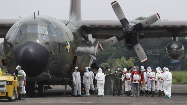 Petugas Palang Merah Indonesia (PMI) menyemprotkan cairan disinfektan kepada kru pesawat Hercules C-130 setibanya di Landasan Udara (Lanud) Halim Perdanakusuma, Jakarta, Senin (23/3). [Suara.com/Angga Budhiyanto]