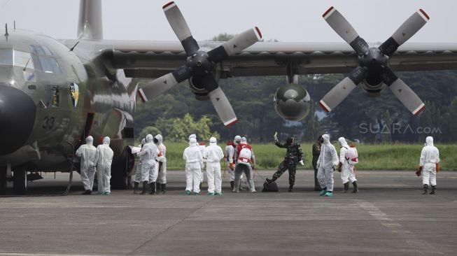 Petugas Palang Merah Indonesia (PMI) menyemprotkan cairan disinfektan ke tas kru pesawat Hercules C-130 setibanya di Landasan Udara (Lanud) Halim Perdanakusuma, Jakarta, Senin (23/3). [Suara.com/Angga Budhiyanto]