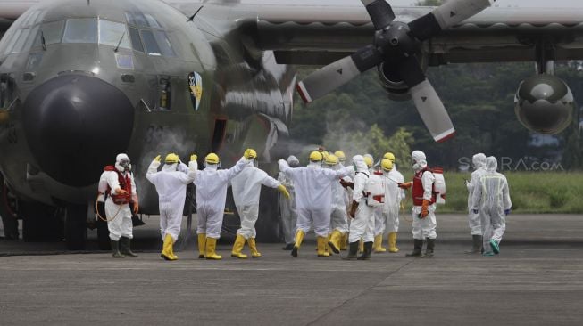 Petugas Palang Merah Indonesia (PMI) menyemprotkan cairan disinfektan kepada kru pesawat Hercules C-130 setibanya di Landasan Udara (Lanud) Halim Perdanakusuma, Jakarta, Senin (23/3). [Suara.com/Angga Budhiyanto