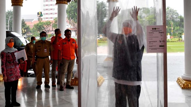 Gubernur Jawa Tirmur Khofifah Indar Parawansa (kanan) memasuki bilik disinfektan atau bilik sikat Corona (Sico) ketika memasuki Gedung Negara Grahadi di Surabaya, Jawa Timur, Senin (23/3).  [ANTARA FOTO/Zabur Karuru]
