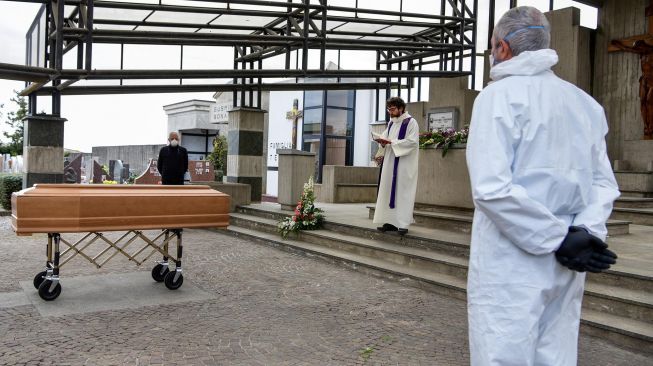 Seorang pendeta membacakan doa saat upacara pemakaman warga yang meninggal di pemakaman Grassobbio, Lombardia, Italia, Selasa (24/3).  [Piero CRUCIATTI / AFP]
