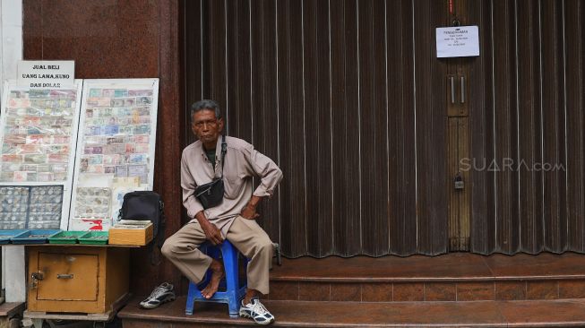 Pedagang uang kuno menggelar dagangannya di depan toko yang tutup di Pasar Baru, Jakarta, Rabu (25/3). [Suara.com/Alfian Winanto]