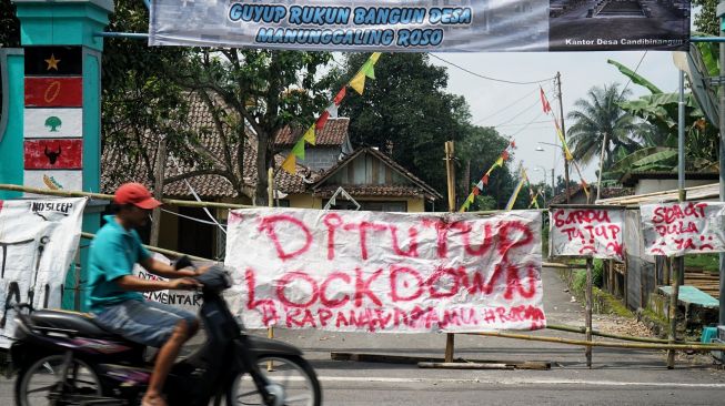 Warga melintas di dekat akses masuk kampung yang ditutup di kawasan Pakem, Sleman, D.I Yogyakarta, Jumat (27/3). [ANTARA FOTO/Andreas Fitri Atmoko]