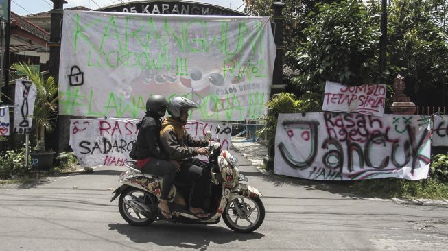 Warga melintas di depan spanduk penutupan jalan masuk Desa Karangwuni, Depok, Sleman, DI Yogyakarta, Senin (30/3). [ANTARA FOTO/Hendra Nurdiyansyah]