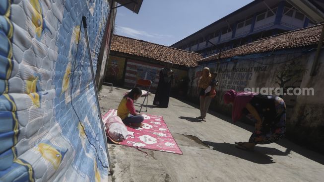 Sejumlah warga berjemur di bawah sinar matahari pagi di Gang Haji Sairan, Kelurahan Jati Padang, Pasar Minggu, Jakarta Selatan, Selasa (31/1).  [Suara.com/Angga Budhiyanto]