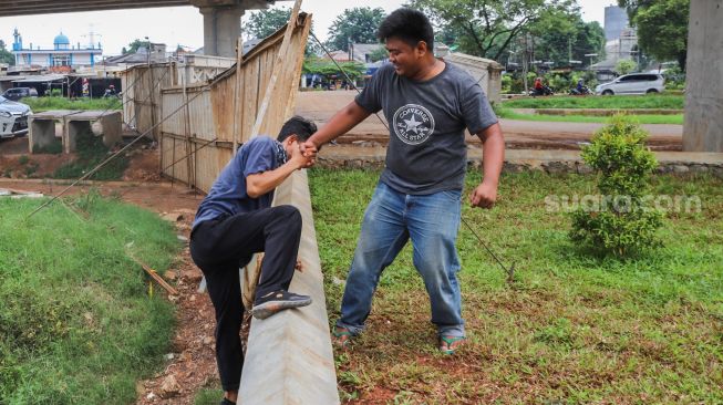 Warga saling membantu memanjat tembok karena akses jalan yang ditutup seng di RW 04 Cipinang Melayu, Jakarta Timur, Selasa (31/3). [Suara.com/Alfian Winanto]
